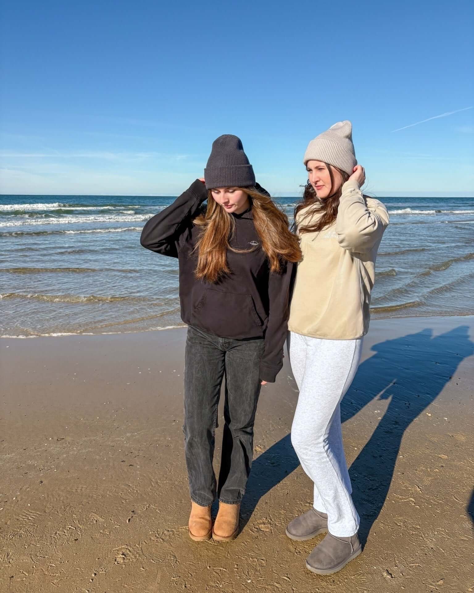 Two women on the beach wearing stylish Beanie | Creme hats and casual attire.