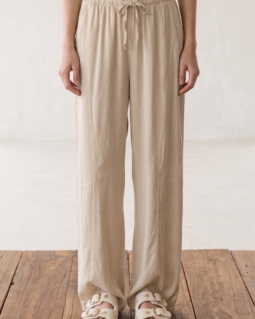 Model trägt Shoreline Palazzohose in Beige, kombiniert mit einem gestreiften Tanktop, ideal für den Sommer.