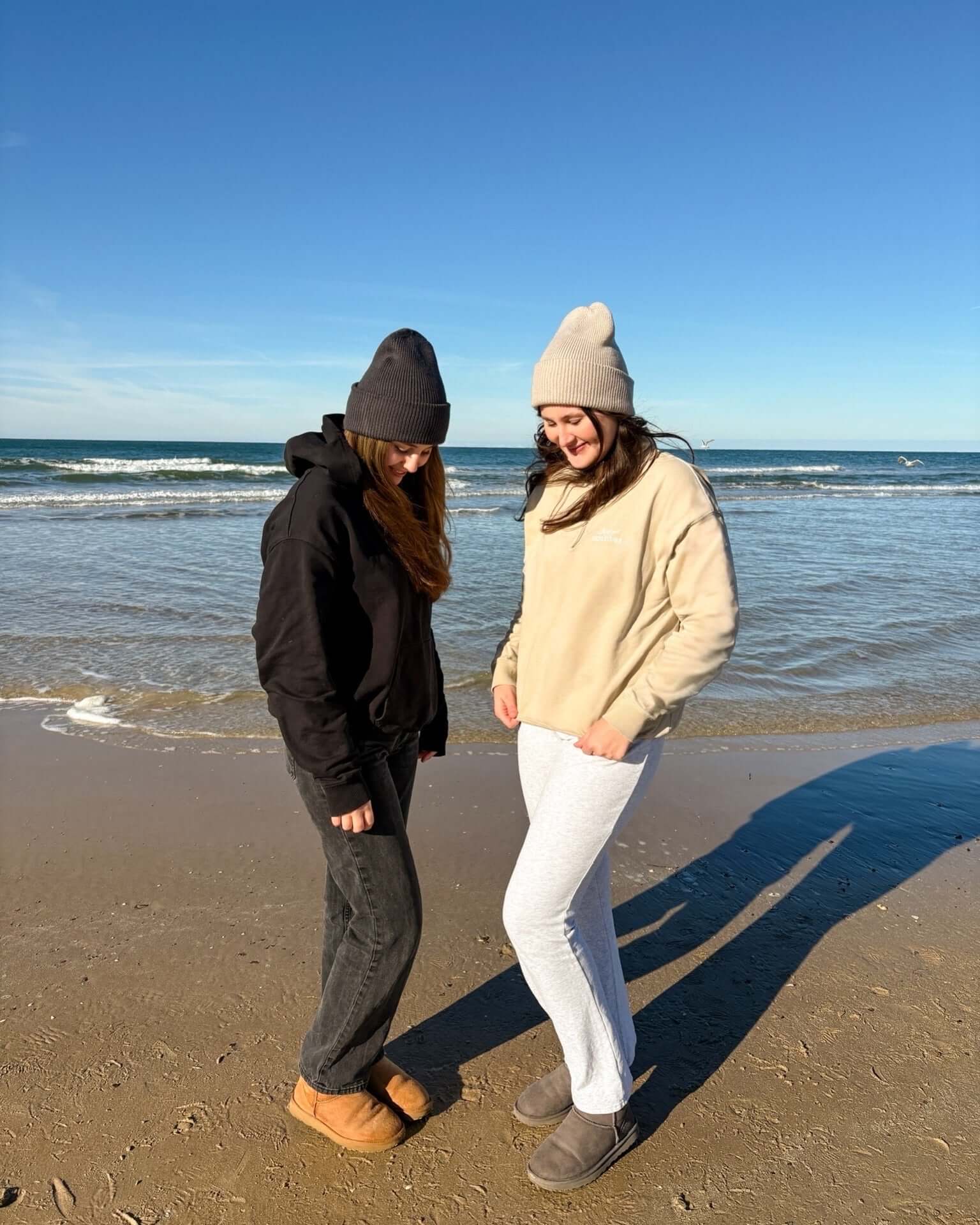 Two women wearing Beanie | Creme on the beach, enjoying a sunny day by the ocean.