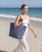 Gestreifte Strandtasche in Navy Stripe, ideal für einen Tag am Strand, während eine Frau am Ufer entlanggeht.