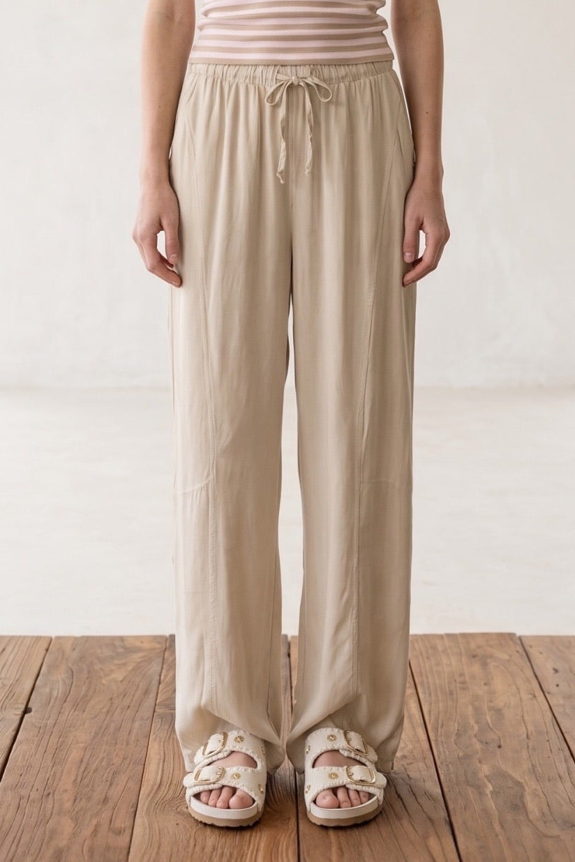 Model trägt Shoreline Palazzohose in Beige, kombiniert mit einem gestreiften Tanktop, ideal für den Sommer.
