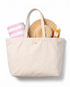 Weiße Strandtasche mit Handtuch, Sonnencreme und Sonnenhut darin, perfekt für den Strandurlaub, 