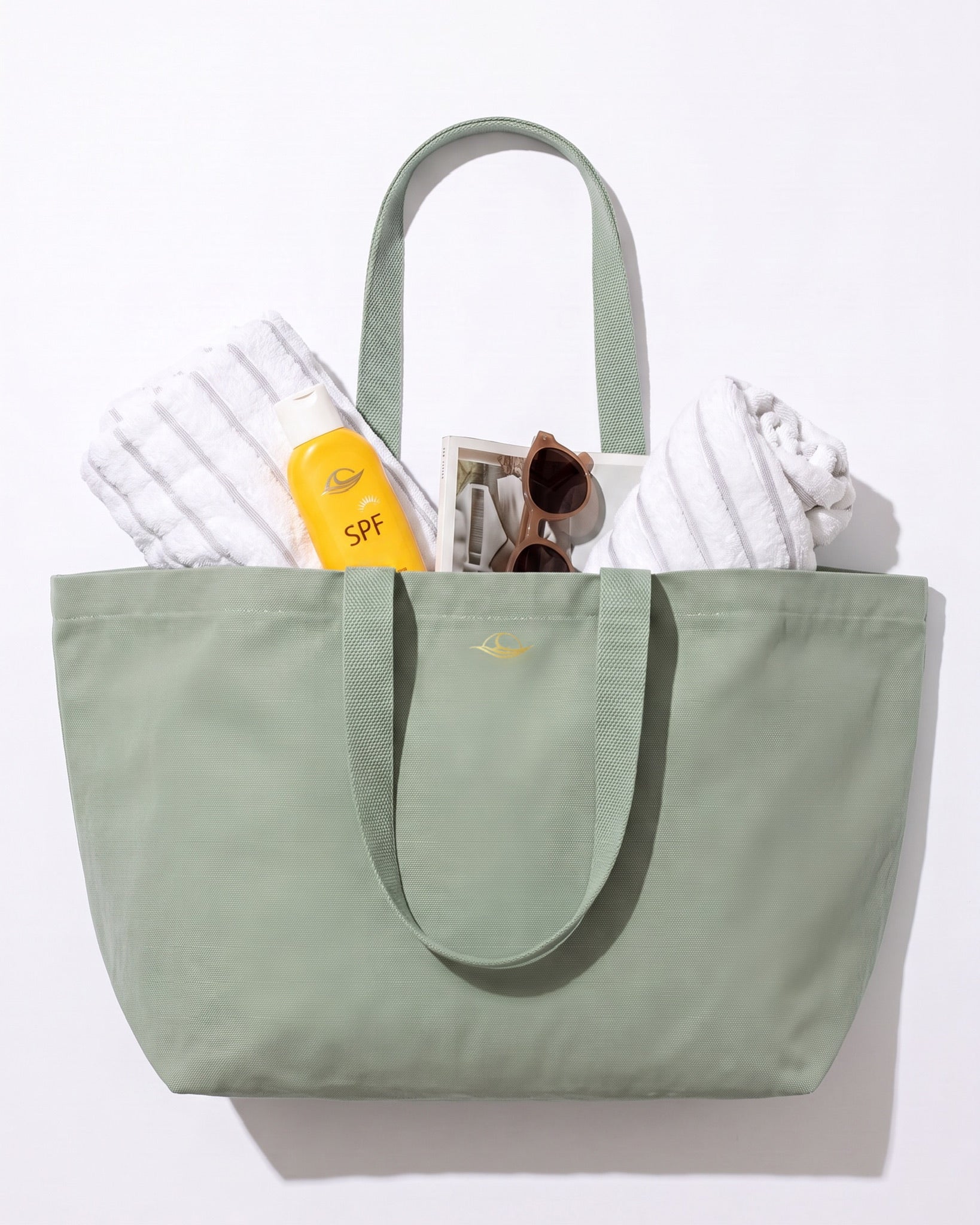 Soleil Strandtasche in Pistazie, gefüllt mit Handtüchern, Sonnencreme und Sonnenbrille.